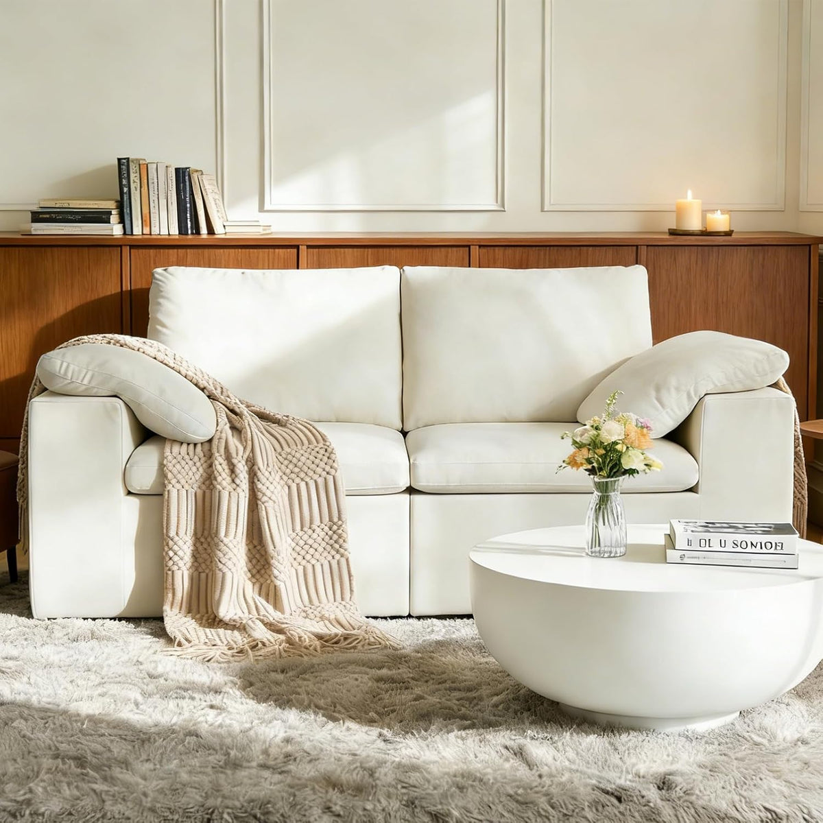 Cream/off-white two-seat sofa staged in a sunny living room with knit throw and round white coffee table.