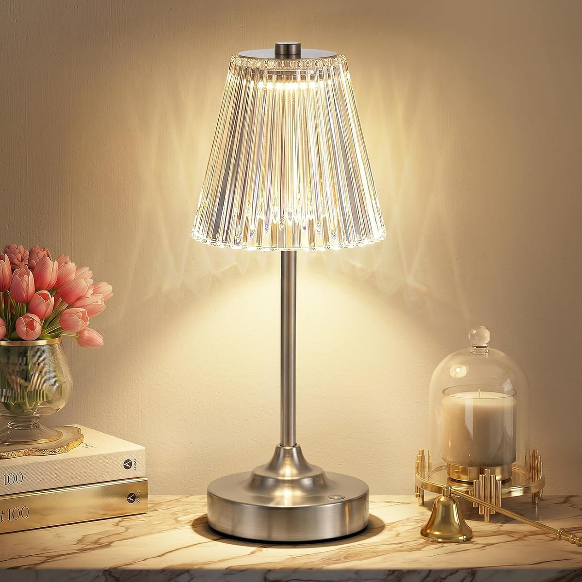 Lamp with brushed silver stem and base beneath an illuminated fluted acrylic shade on a bedside surface
