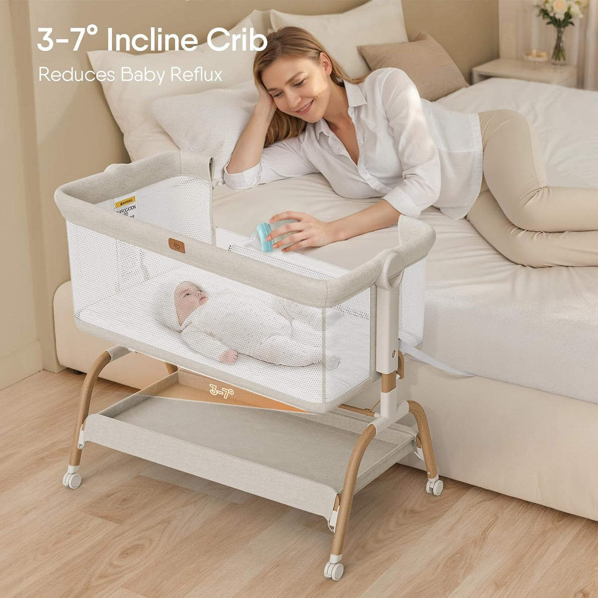 Side view of the bassinet attached to a bed with a mother reaching over while a baby lies inside the mesh-sided bassinet.