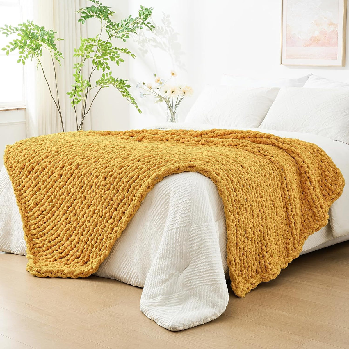 Golden mustard chunky knit throw spread over a white quilted bed in a sunlit room