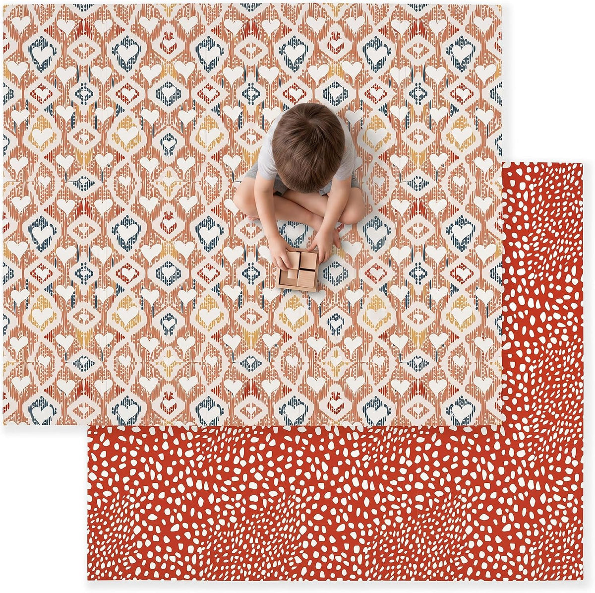 Overhead view of a child sitting on a rust-and-cream patterned mat with red reversible underside