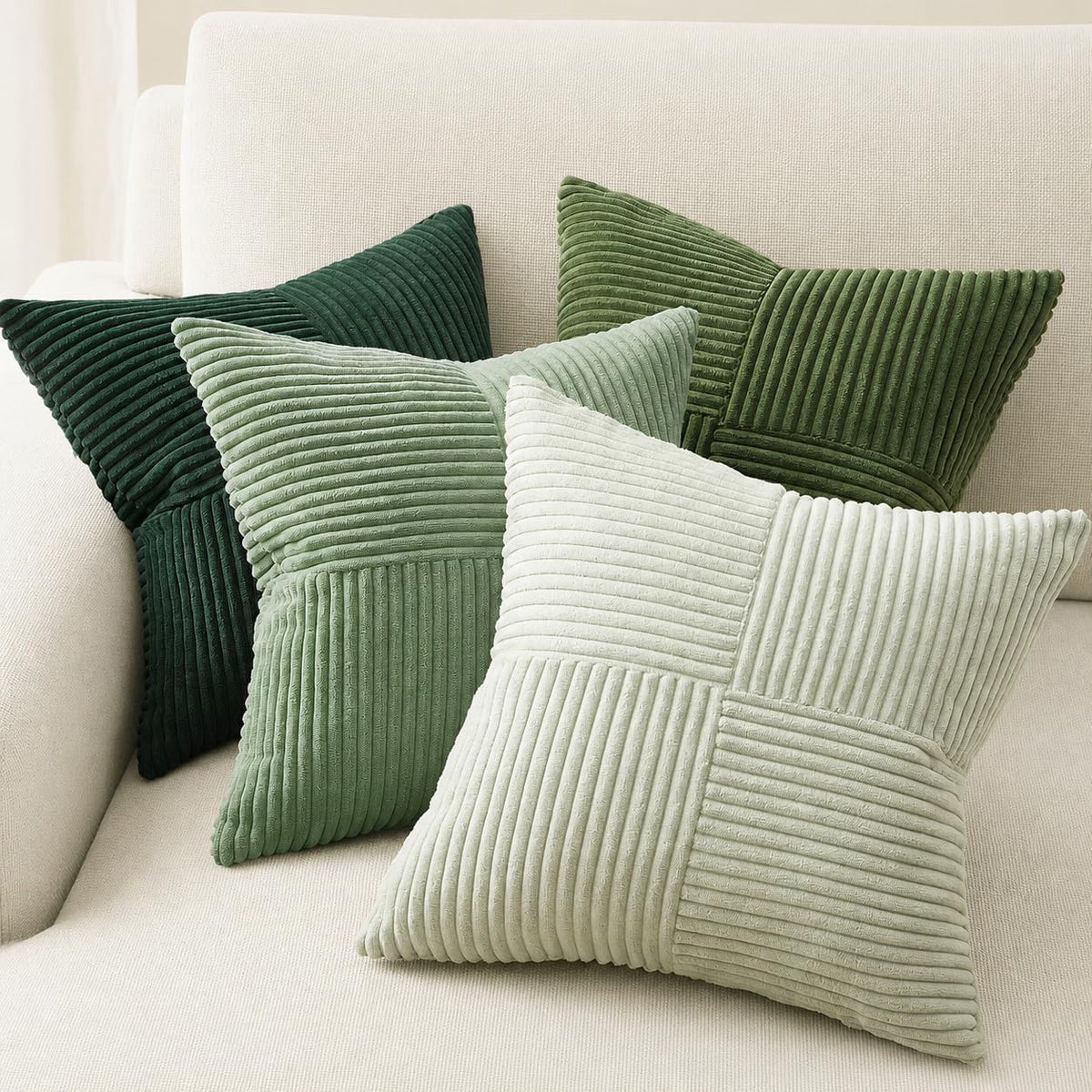 Four green-tone corduroy patchwork pillow covers in varying shades on a couch.
