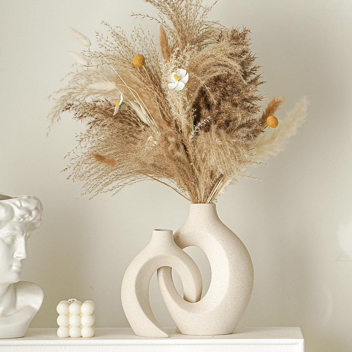 Two matte beige sculptural vases styled on a mantel with pampas grass and decorative bust