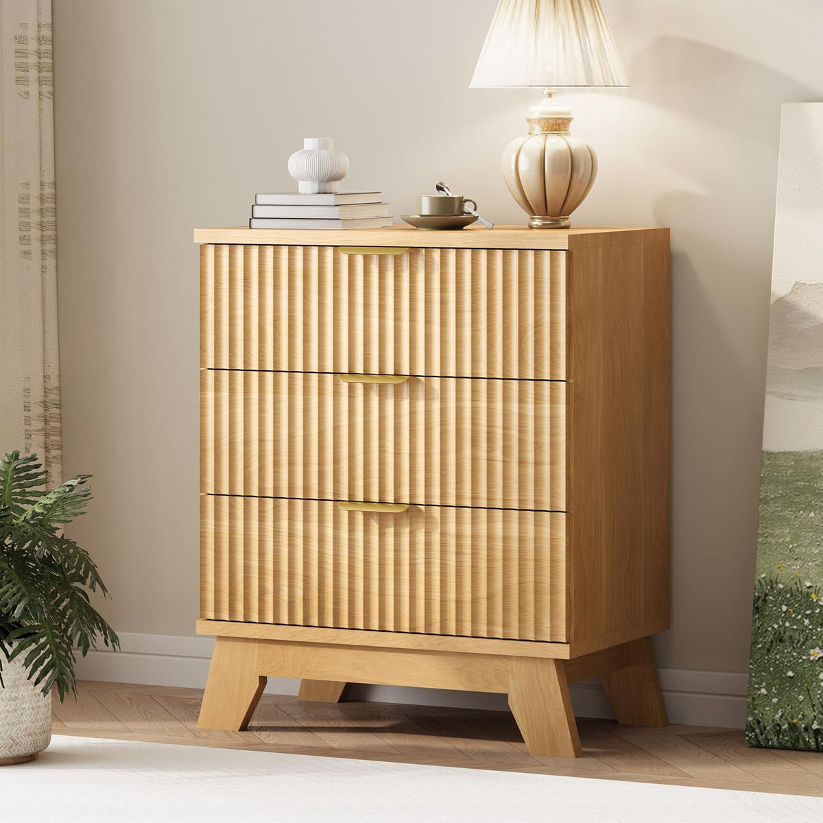 Three-drawer tall chest in light wood with vertical wave panels and gold metal handles, lamp on top.