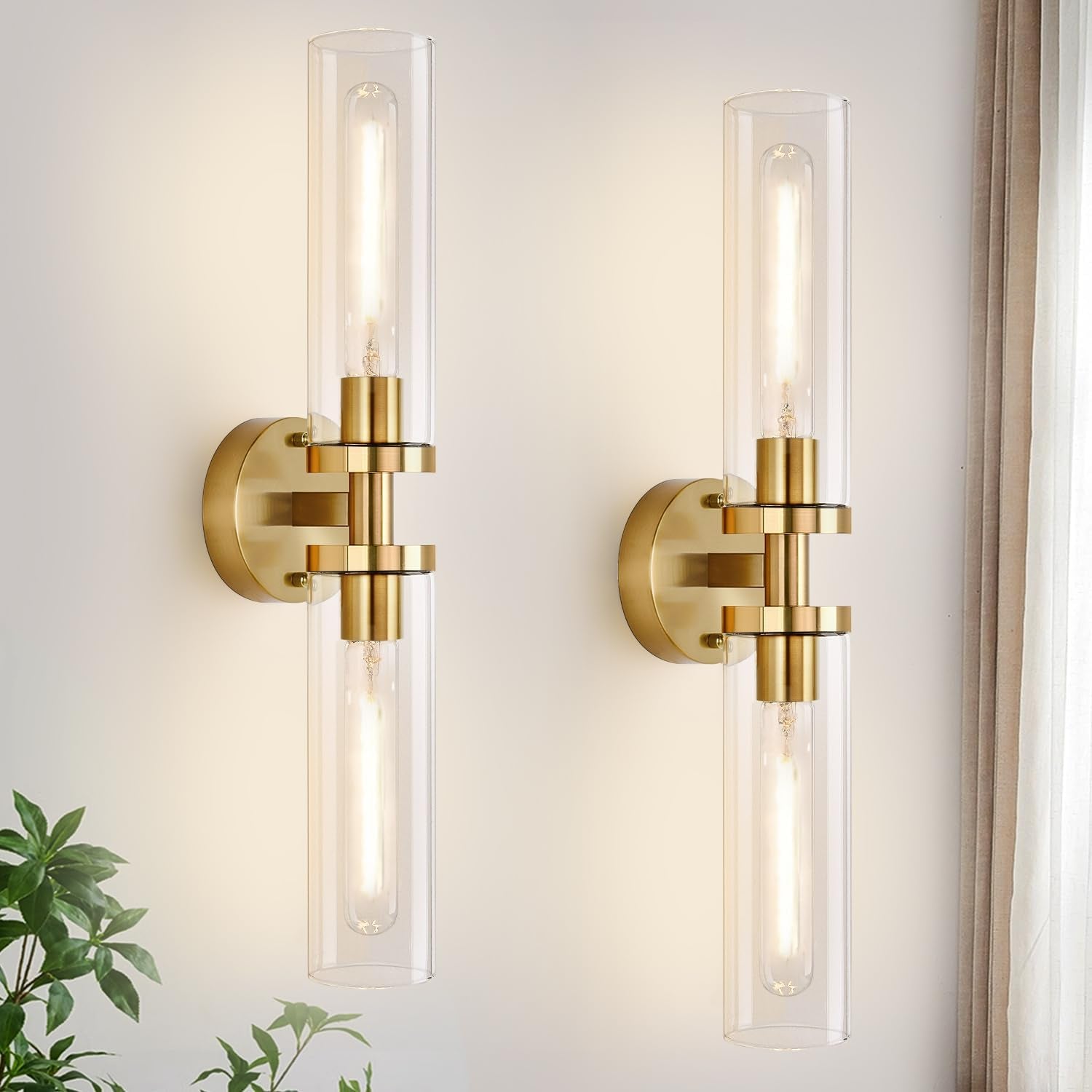 Pair of vertical brushed-gold wall sconces with clear cylindrical glass shades on a light wall.