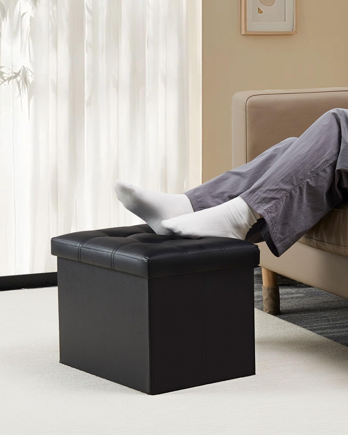 Living room scene showing a person resting socked feet on a black tufted ottoman next to a beige sofa.