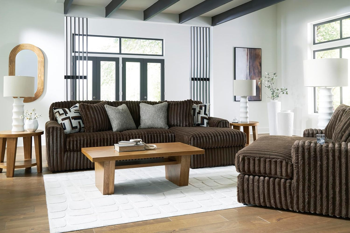 Living room scene with oversized brown corduroy sofa and chaise amid wood tables and white lamps