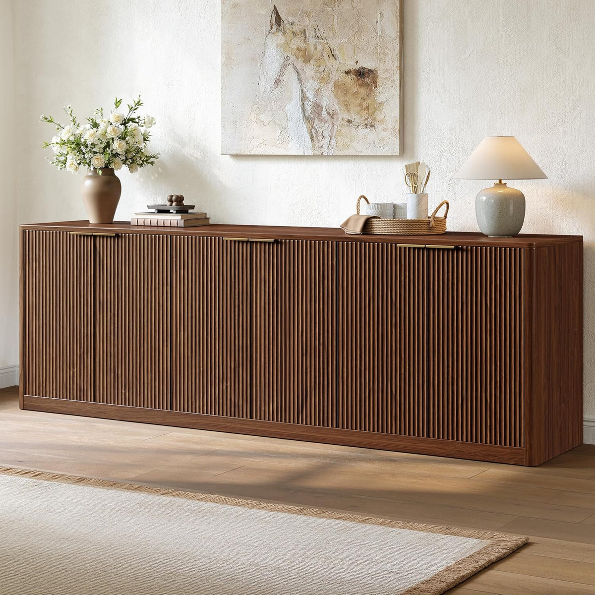 Long closed walnut buffet with vertical fluted doors styled with vase, tray and lamp on top.