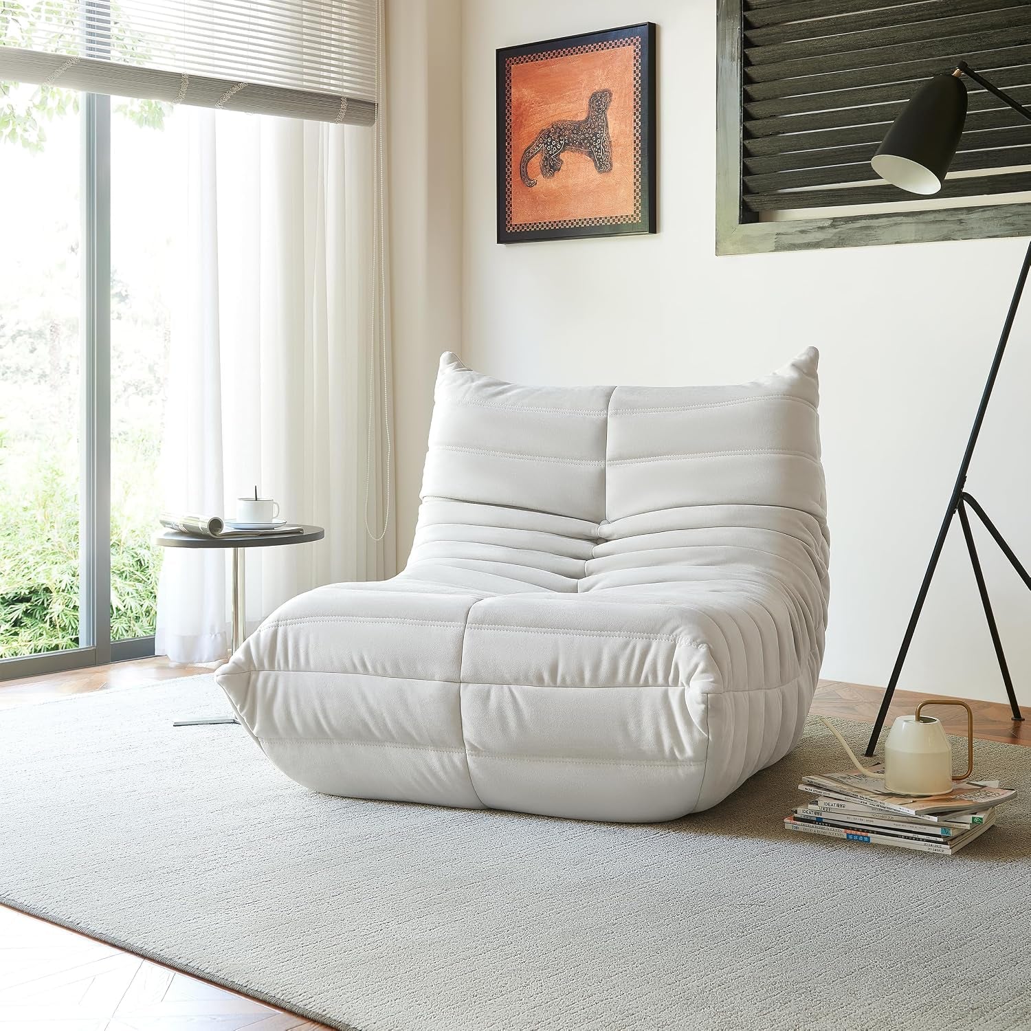 Light gray single bean bag chair near a window, styled with a teacup on a metal side table and a low lamp nearby.