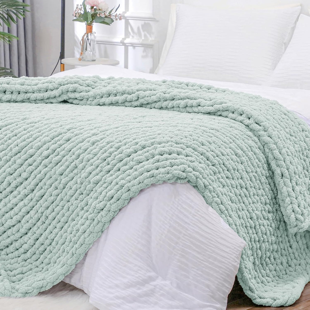 Close view of a chunky mint-green knit throw draped across a white bed, showing thick braided texture.