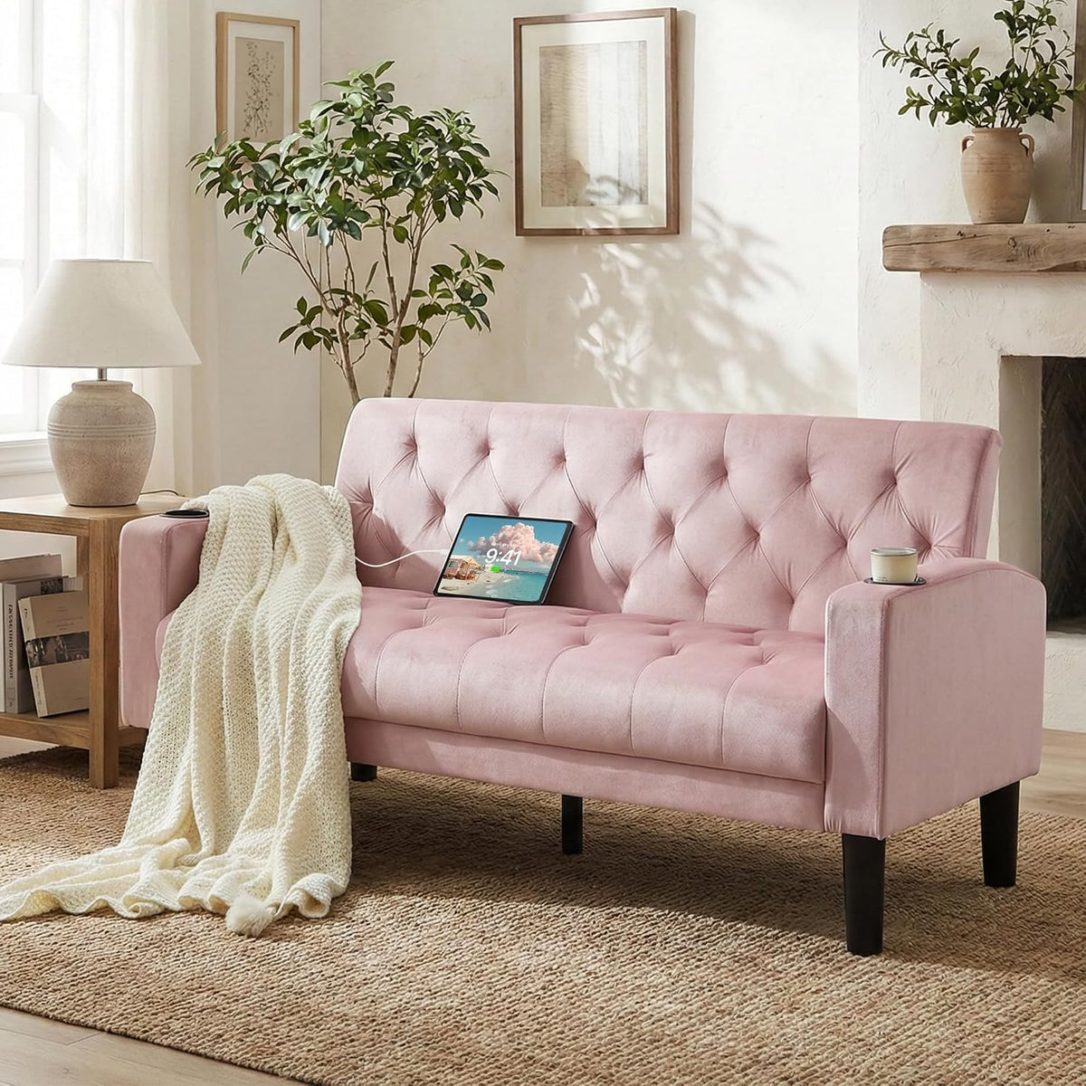 Soft pink tufted loveseat with a knitted throw spilling to the floor and a candle placed in the arm cup holder.