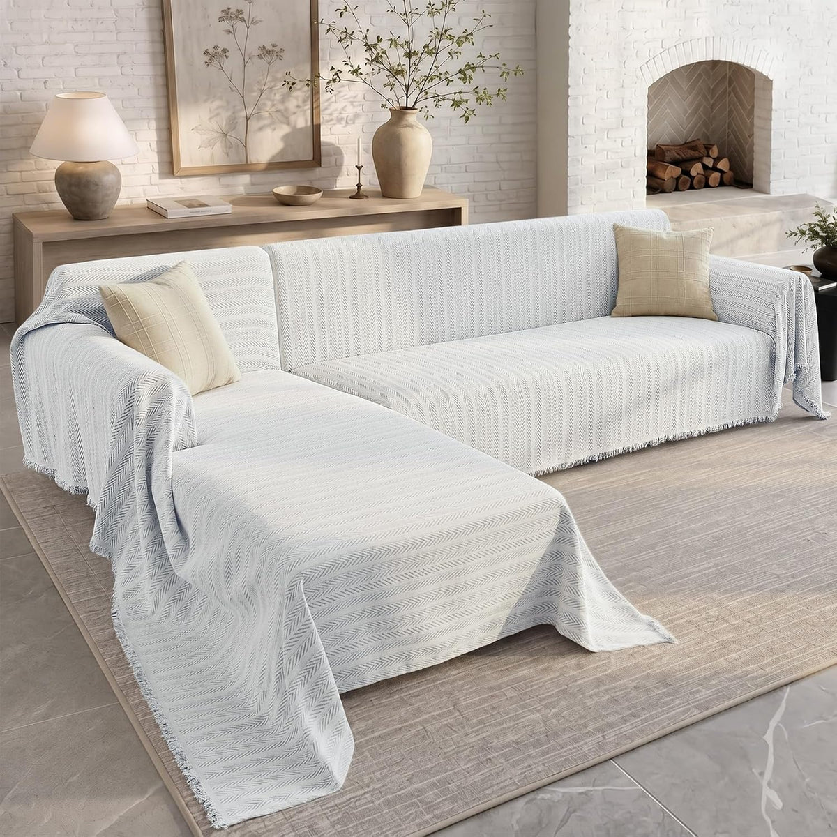 Light-blue tinted cover draped over an L-shaped sofa in a neutral contemporary room with console and vase.