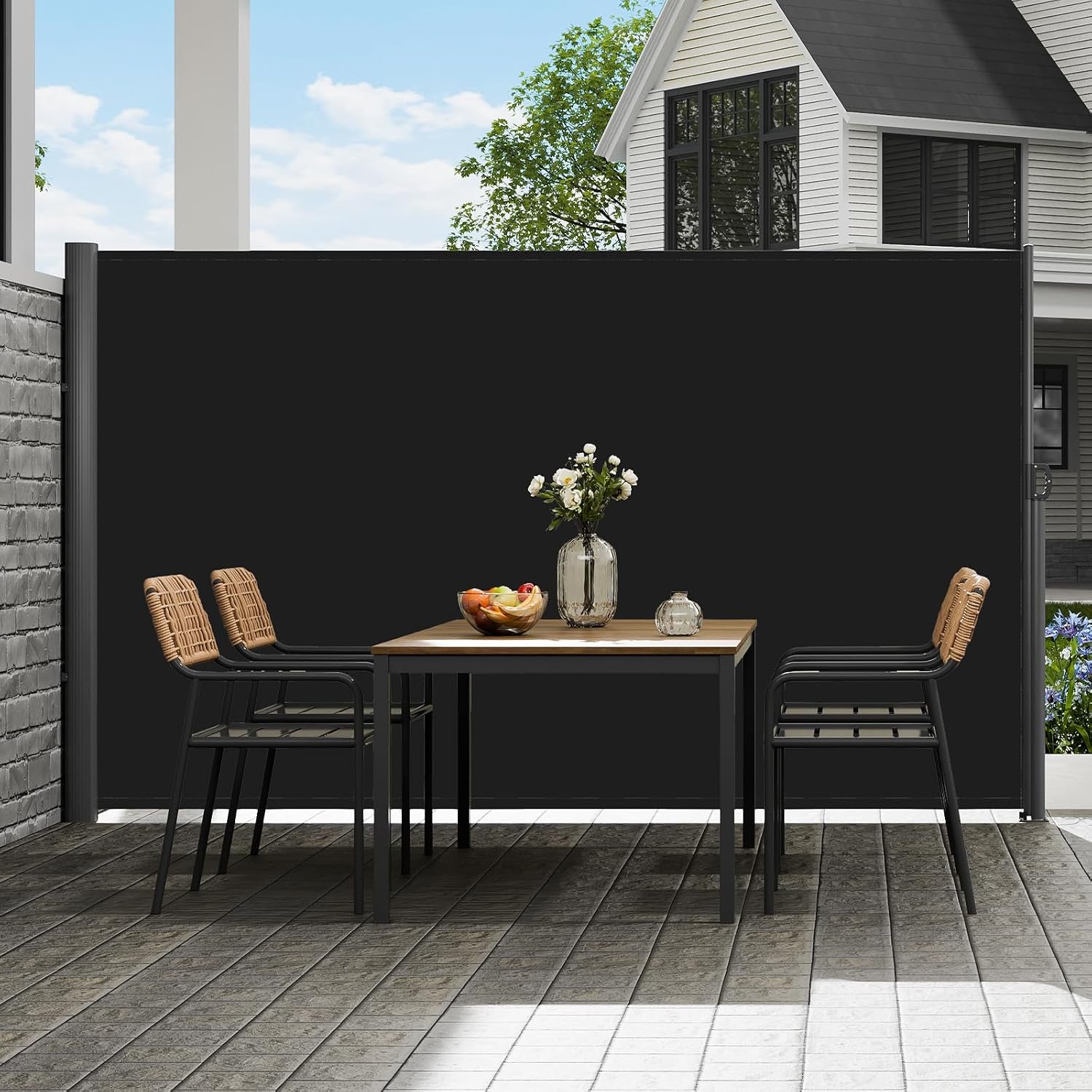 Outdoor dining scene with the black side awning lowered beside a table and chairs, house facade and trees visible in