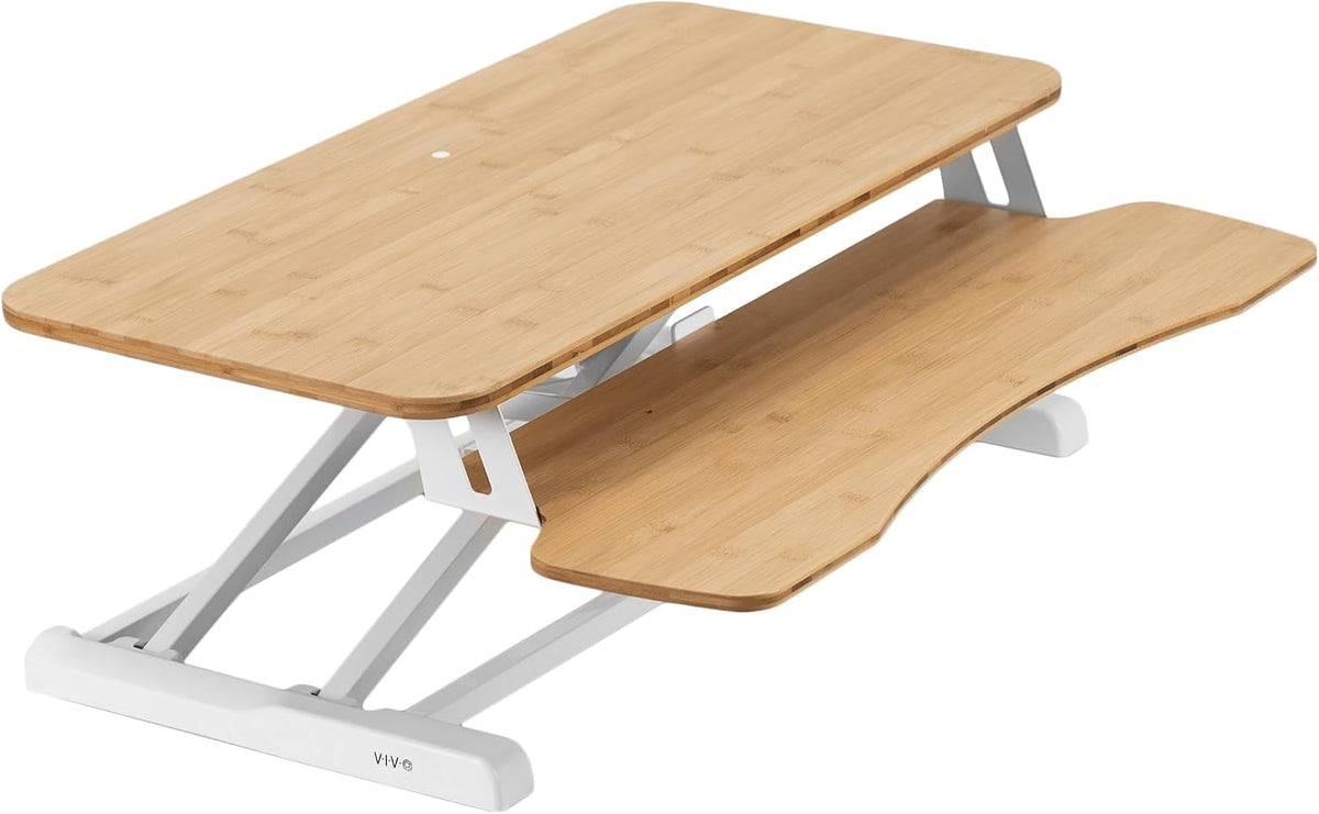 Angled view of a bamboo-finish standing desk converter with white metal frame and keyboard tray
