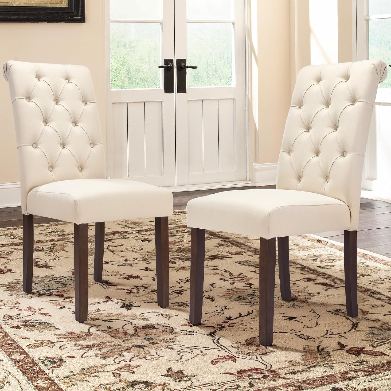 Pair of light taupe tufted dining chairs on a patterned rug in front of French doors.