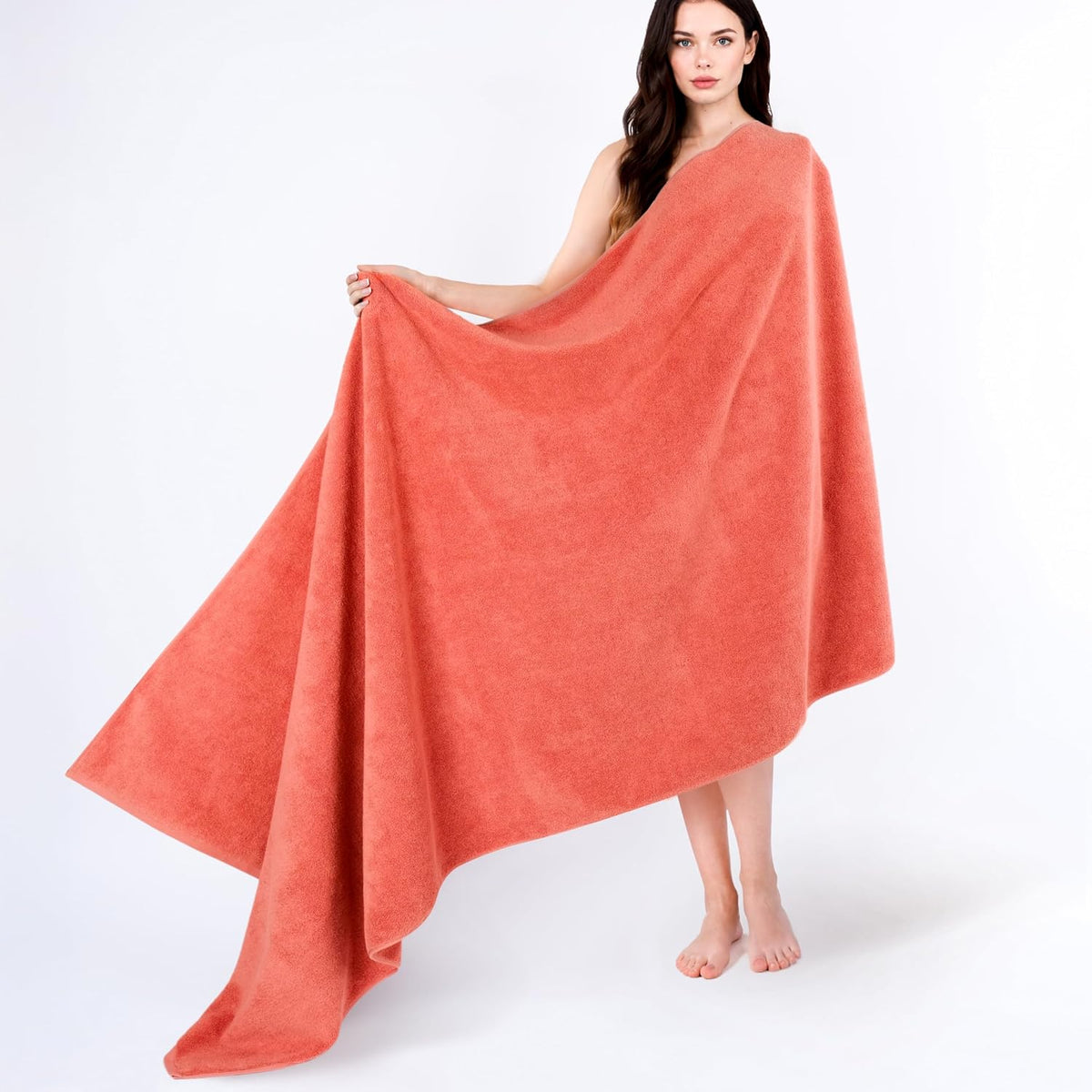 Model standing barefoot holding open a large coral-colored towel draped around her body