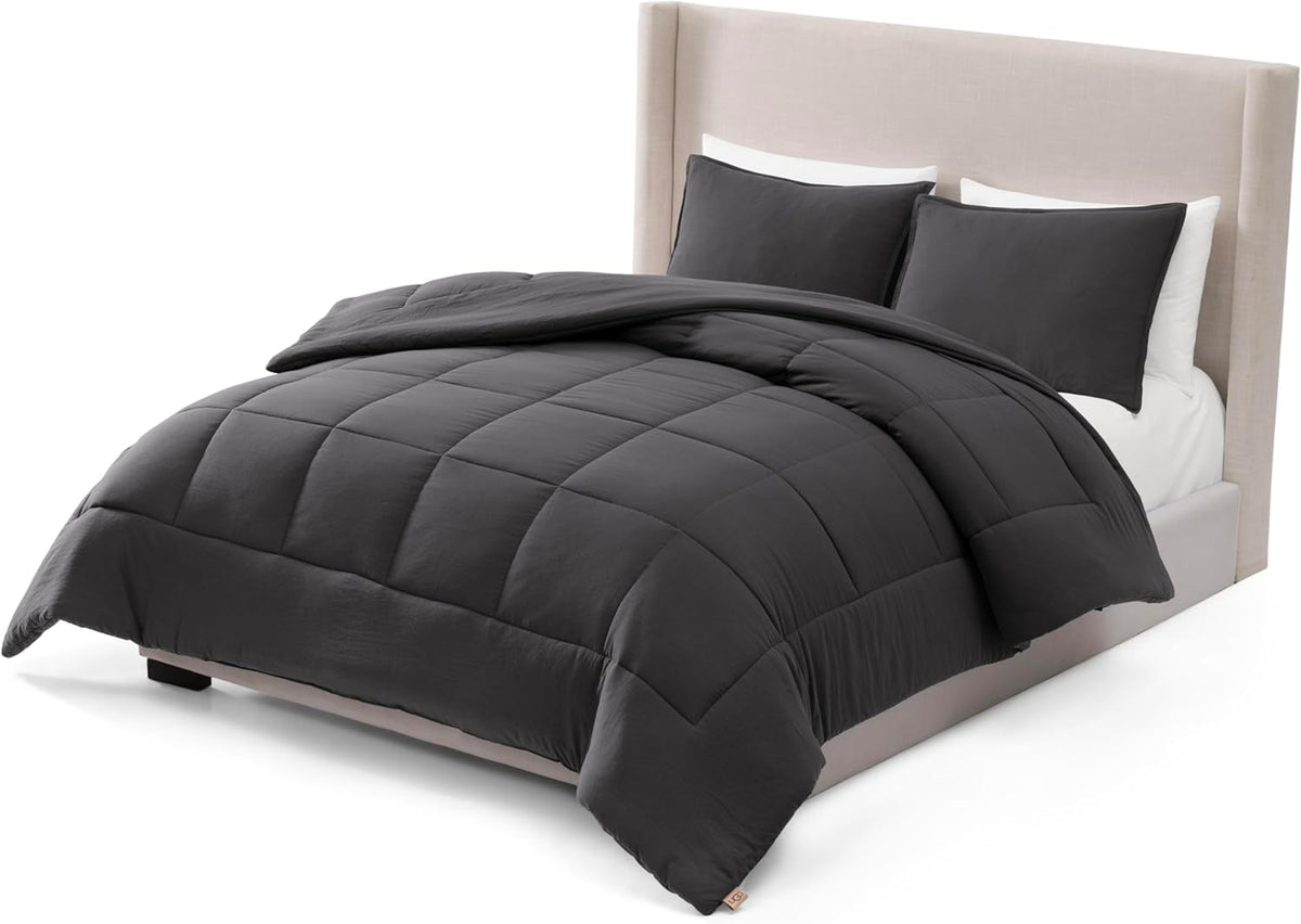 Dark charcoal comforter draped over a made bed with two matching pillow shams and white pillows behind them.