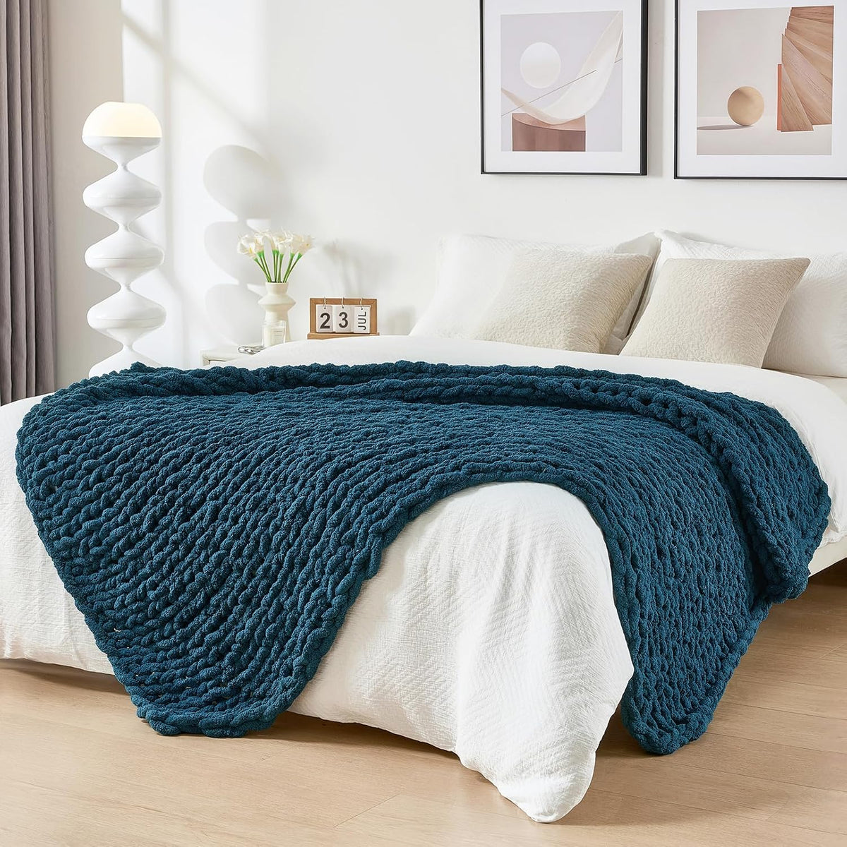 Teal chunky knit throw spread over the foot of a white bed in a minimal bedroom.