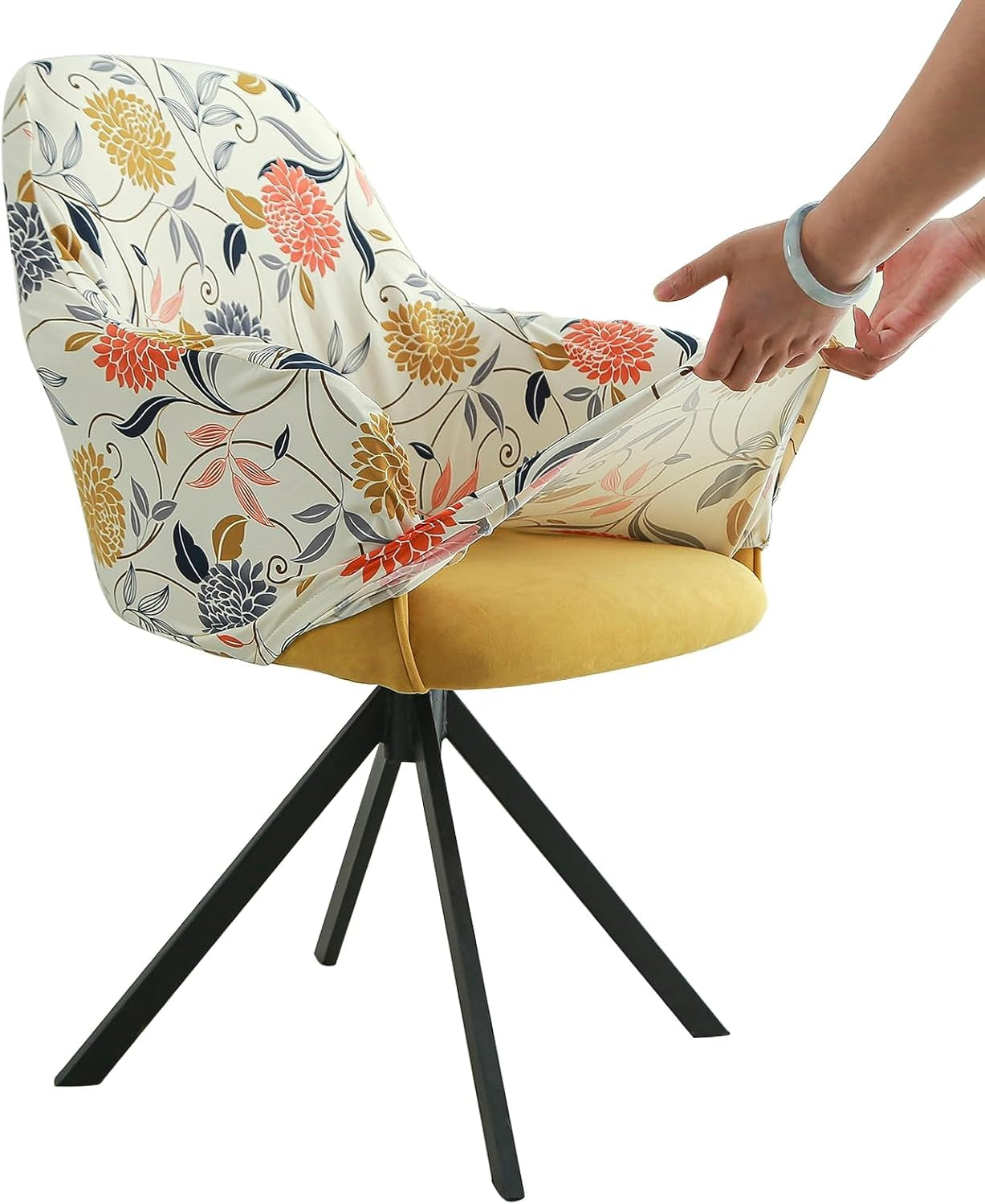 Side view of a cream chair cover with orange and gold floral print being stretched over an armchair by two hands.