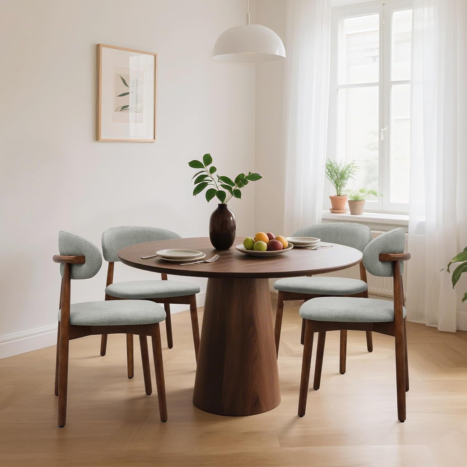 Four pale gray upholstered chairs with brown frames surround a round pedestal dining table.