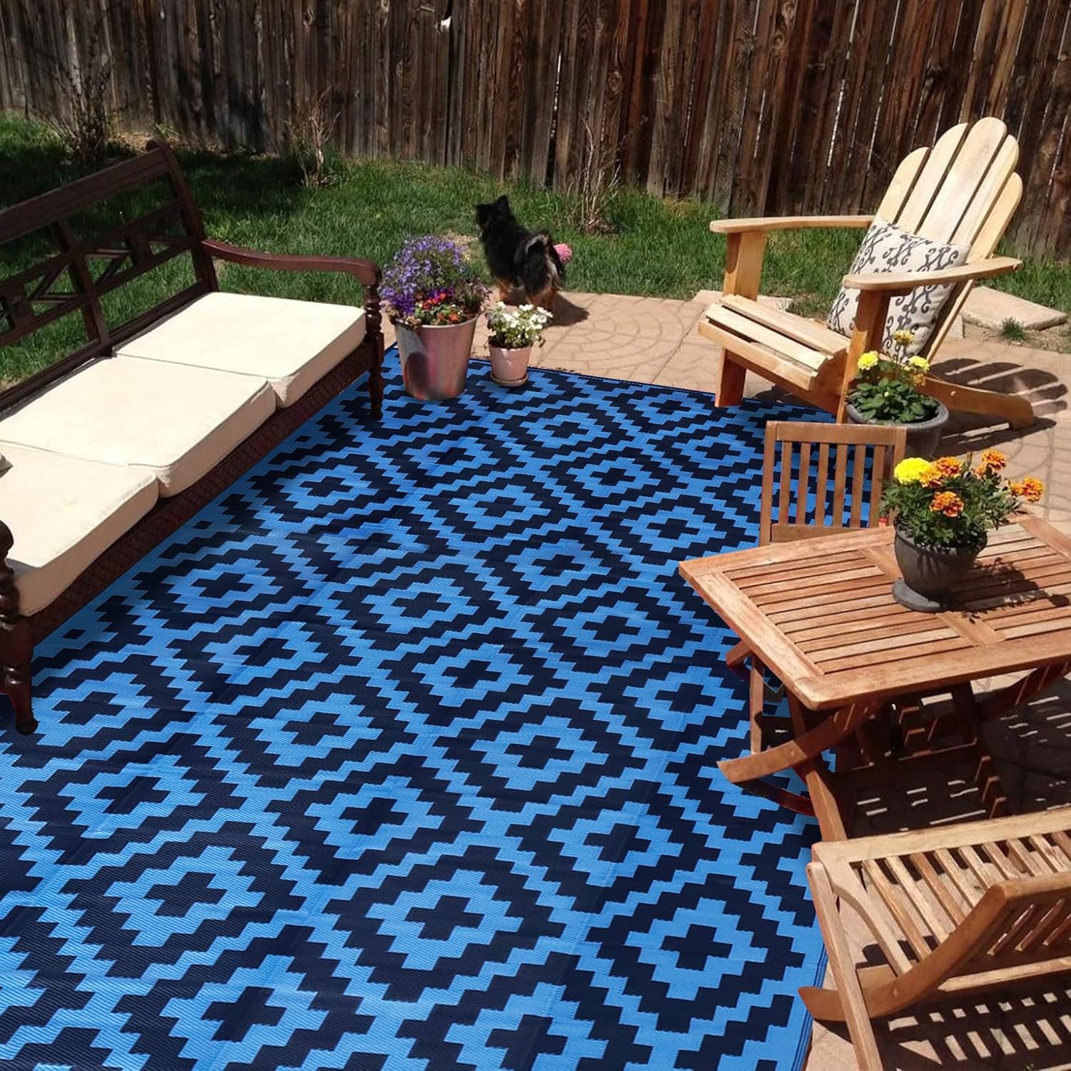 Blue-and-black geometric outdoor rug on a patio with wooden chairs and potted plants