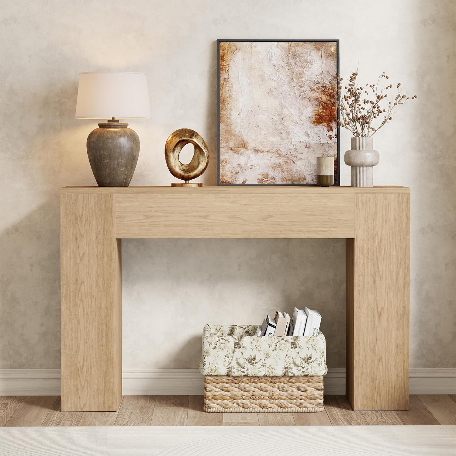 Front view of a pale light-oak console table with lamp, sculpture, framed art and a woven basket below.