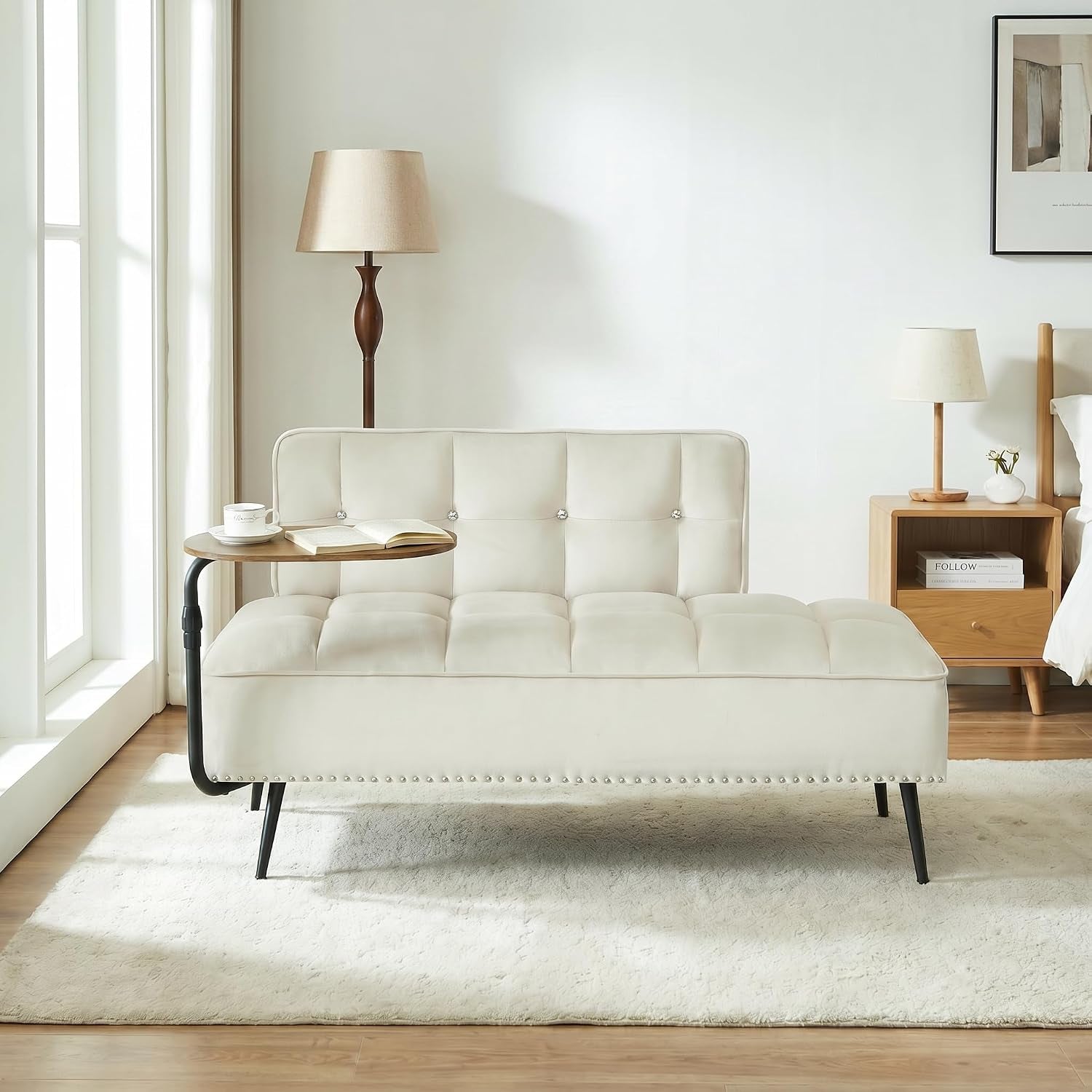 Cream velvet futon sofa in a bright room with a small attached side table and floor lamp.
