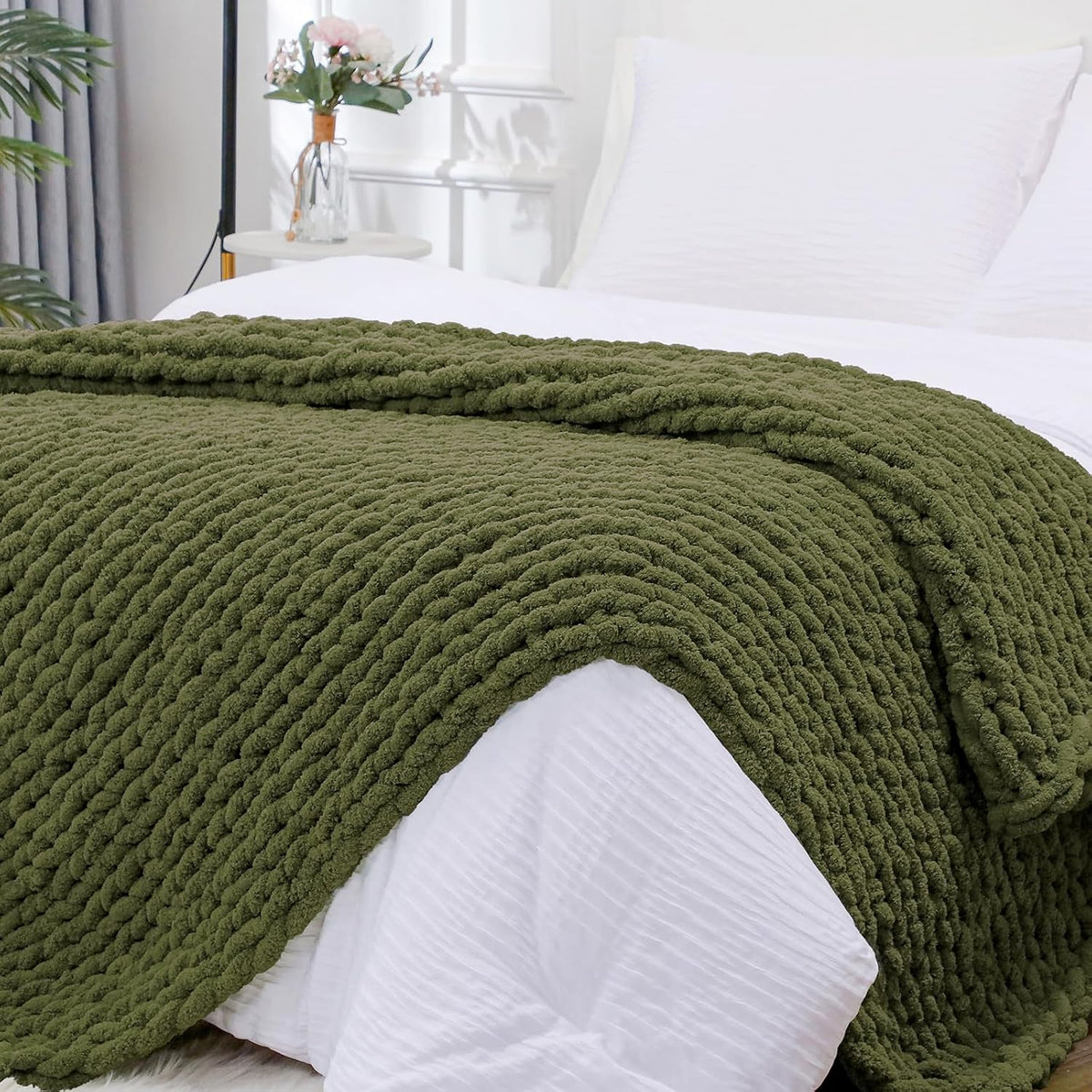 Olive green chunky knit throw smoothed across the foot of a made bed with white linens.