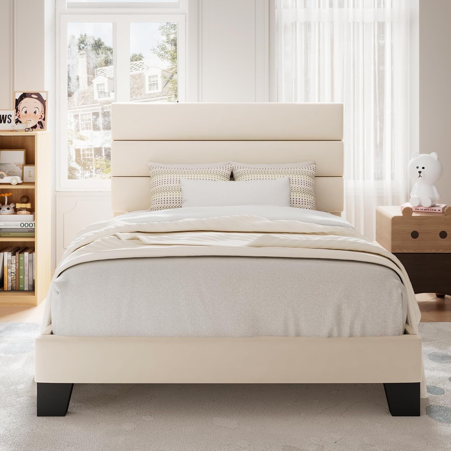 Front bedroom view of a cream upholstered bed with a three-panel headboard and black feet.