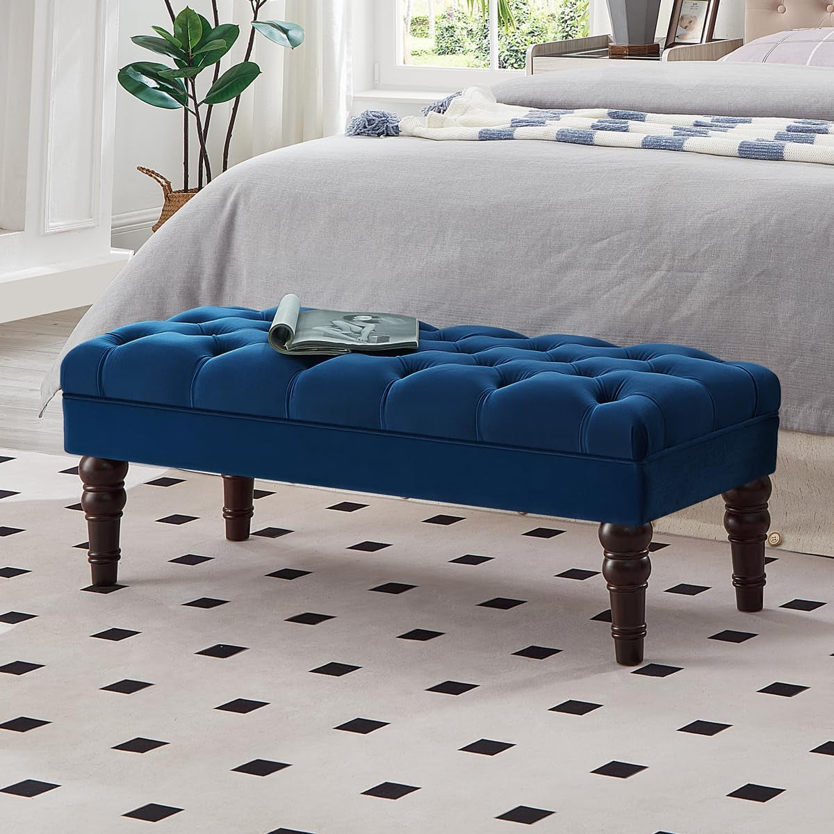 Deep blue velvet tufted bench with turned wooden legs and an open magazine on top at a bedroom end