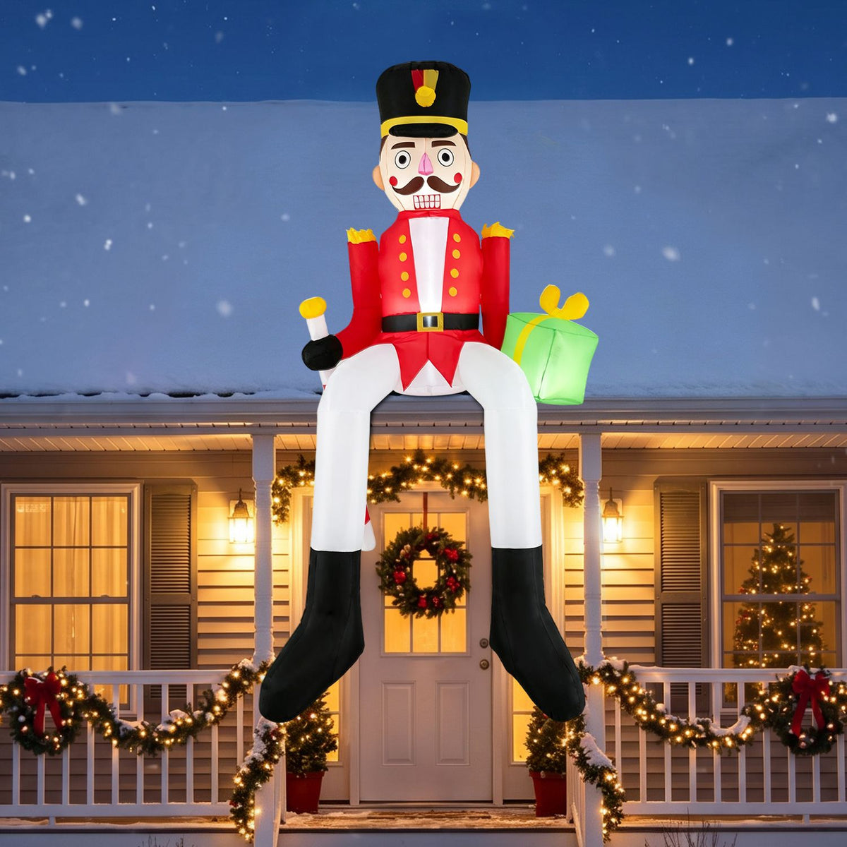 A giant seated nutcracker inflatable hangs above a warmly lit, wreath-decorated porch at night.