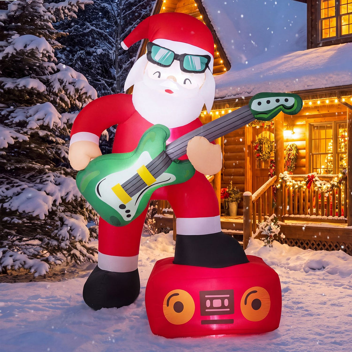 Inflatable Santa in sunglasses plays a green guitar on a red speaker base beside a snowy, lit cabin.