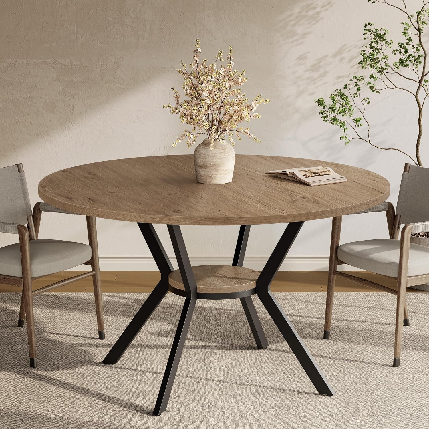 Large round wood-top table with black metal legs and center shelf, styled with vase and chairs