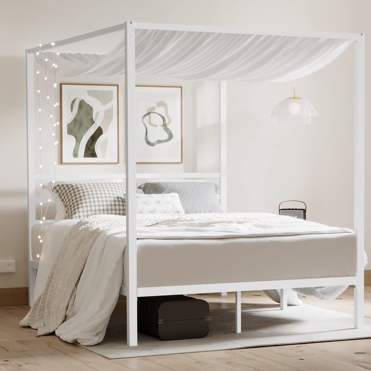 Angled front view of a white metal canopy bed with draped white fabric, fairy lights and a suitcase stored underneath