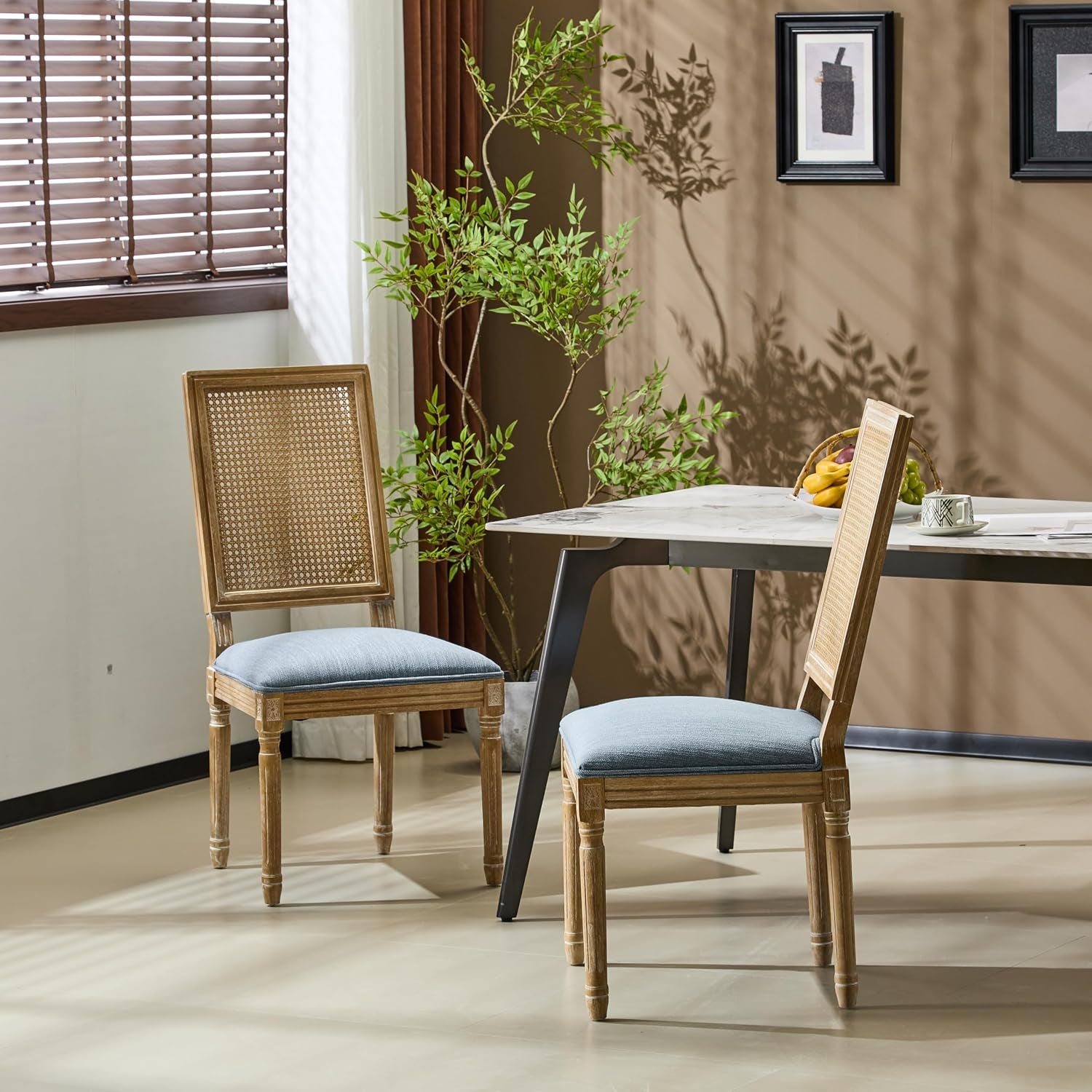 Pair of cane-back chairs with light blue upholstered seats at a dining table with framed wall art