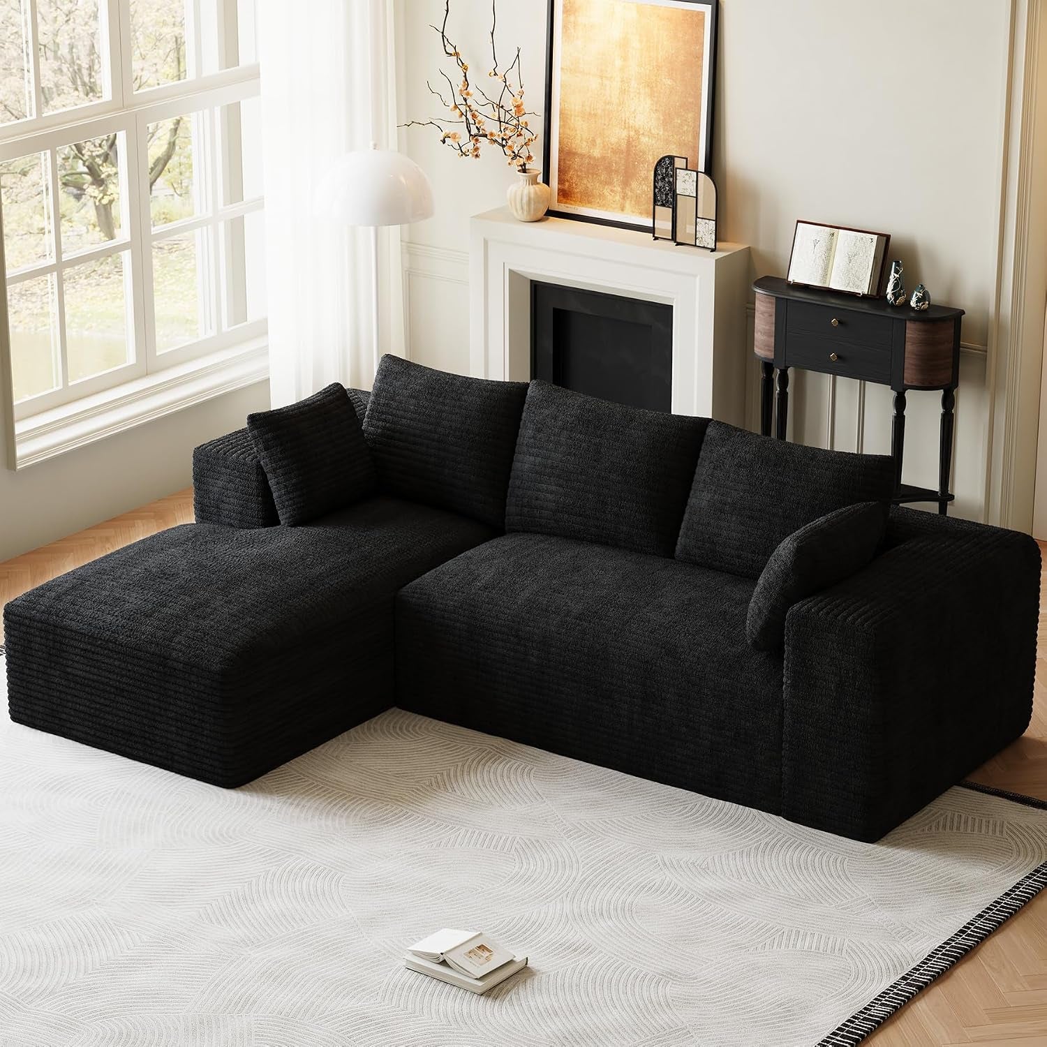 Angled view of a black L-shaped sectional with chaise beside a window and mantel.