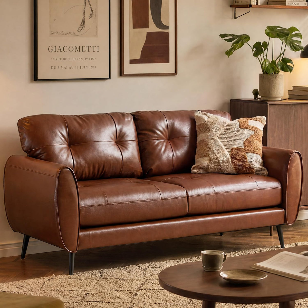 Warm brown faux-leather loveseat with tufted cushions and a textured throw pillow beside a wooden cabinet
