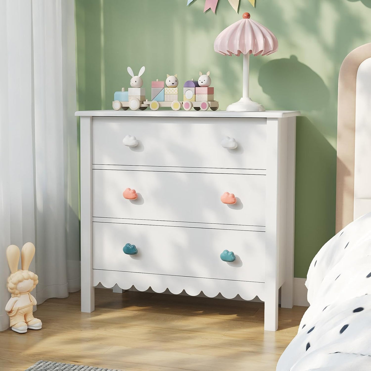White scalloped 3-drawer dresser with mixed cloud-shaped handles at a front-left angle in a child's bedroom