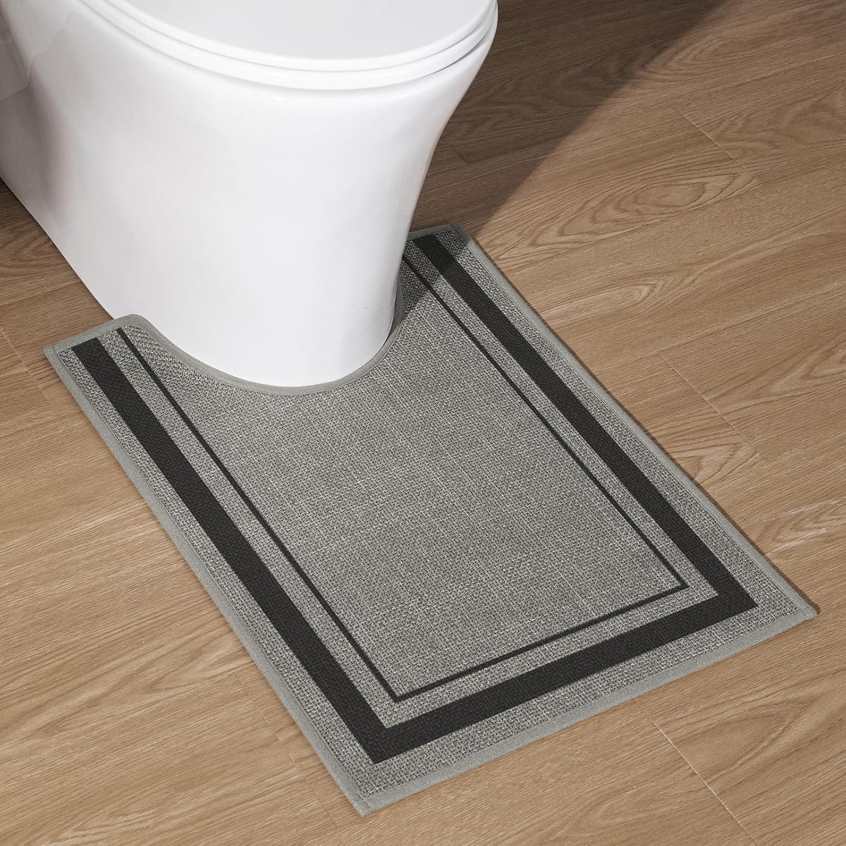 U-shaped toilet contour rug in gray tones placed on wood floor next to a white toilet