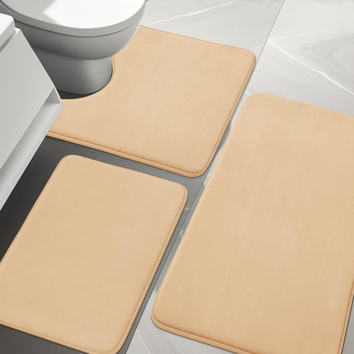 Close view of beige bath rugs on tiled bathroom floor showing toilet cutout and rounded edges