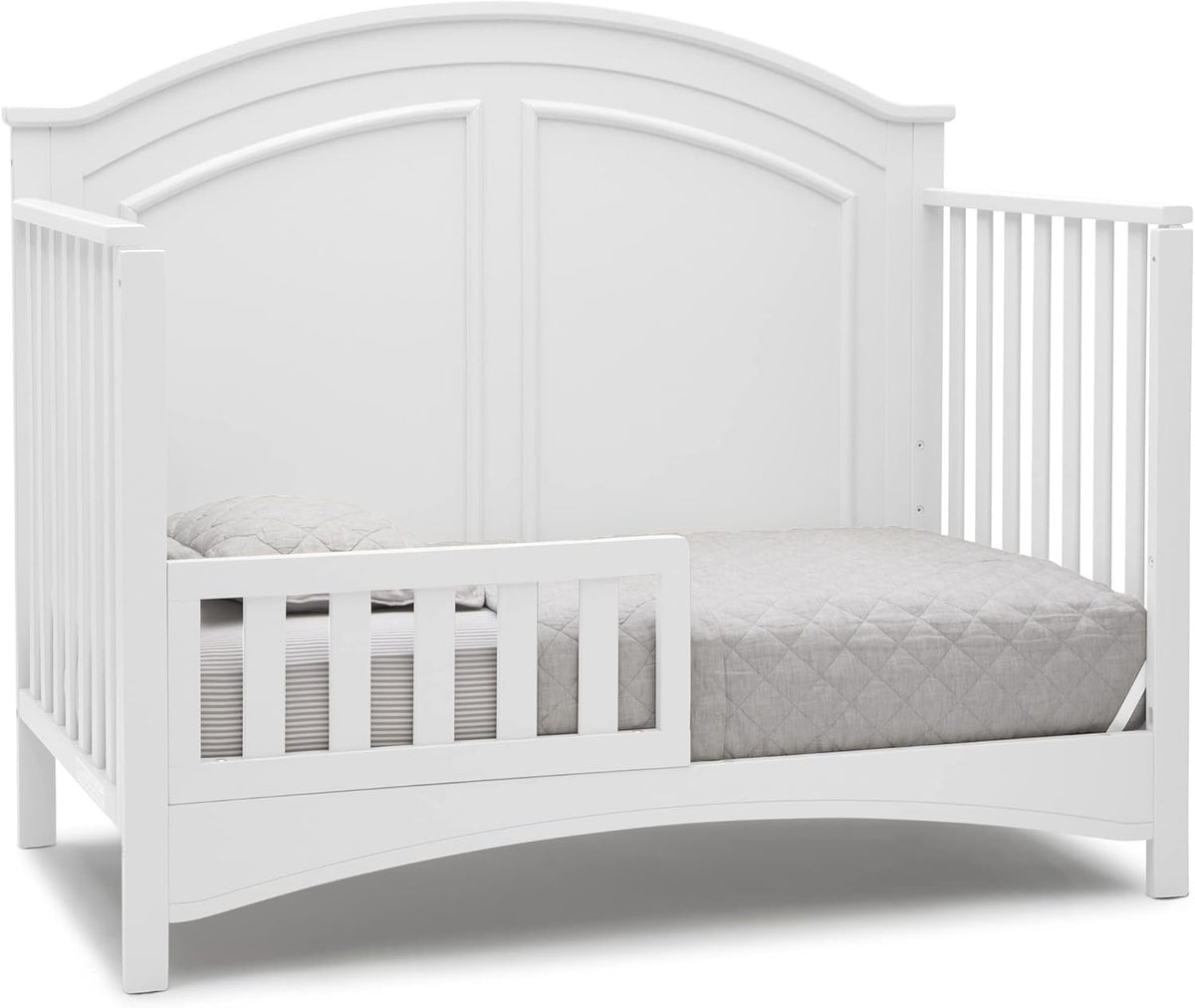 White crib converted with a low toddler rail on one side, showing mattress and quilted bedding