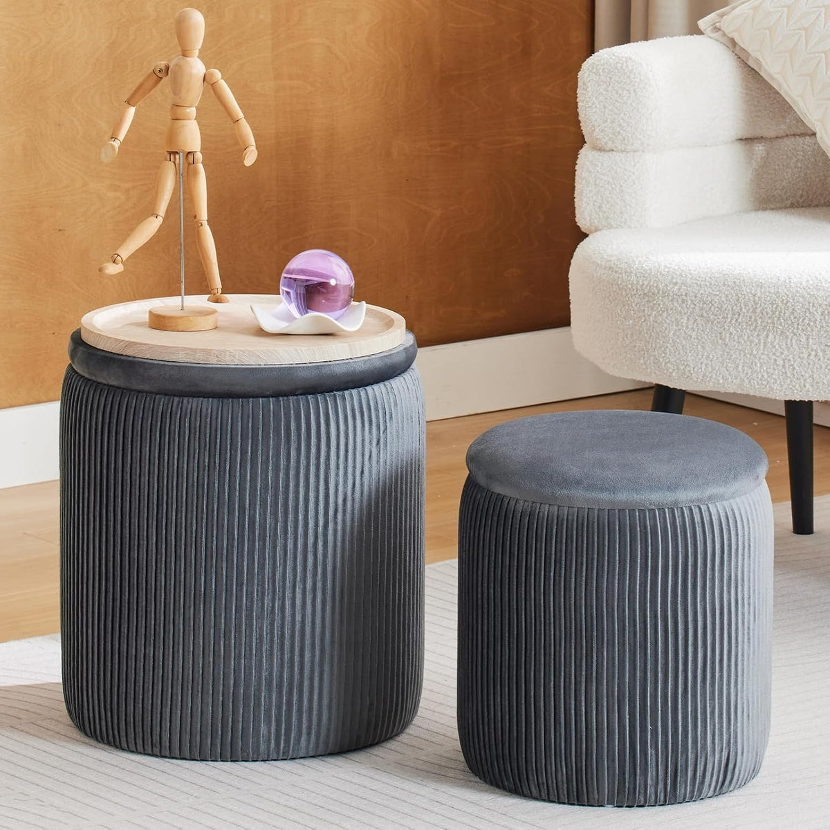 Pair of dark gray ribbed velvet round ottomans, one topped with a light wood tabletop and decorative objects.