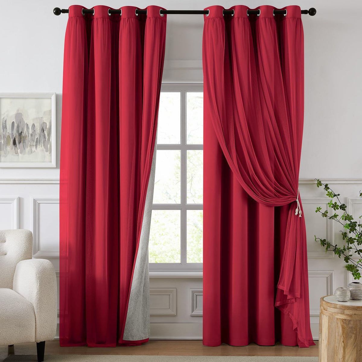 Deep red blackout curtains with a sheer overlay draped and tied at one side in a bright window setting.