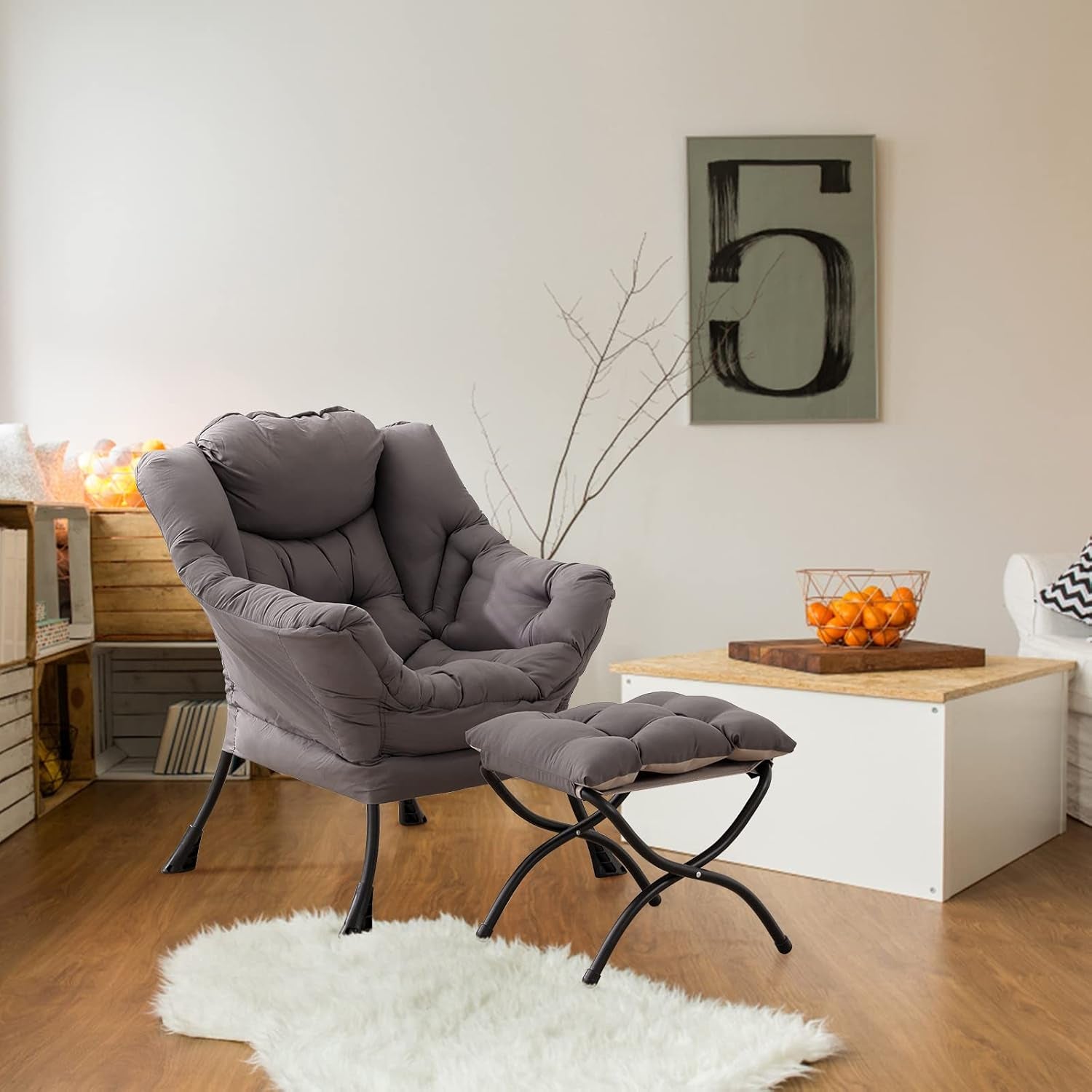 Gray padded lazy chair and ottoman on wood floor next to low table and wall art.