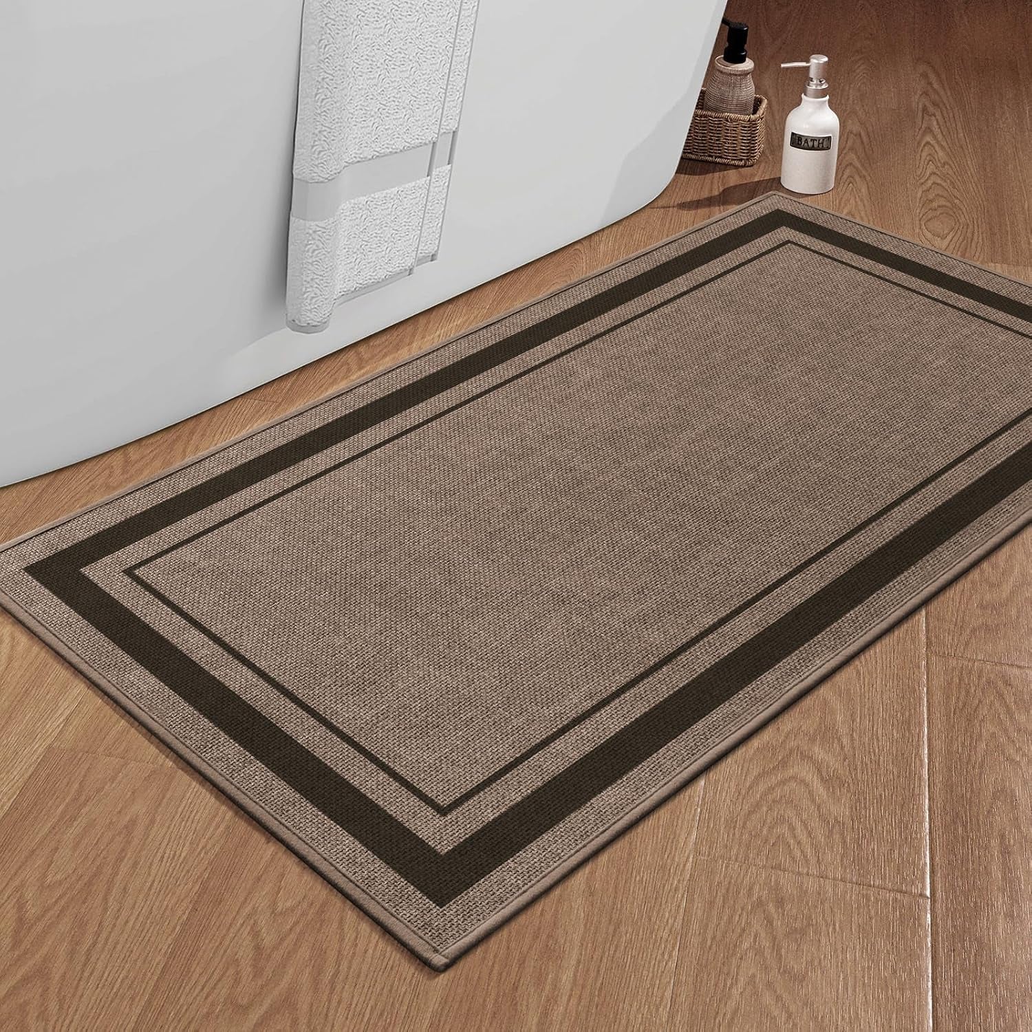 Dark beige rectangular bath rug on wood floor placed beside a white tub and toiletry bottle