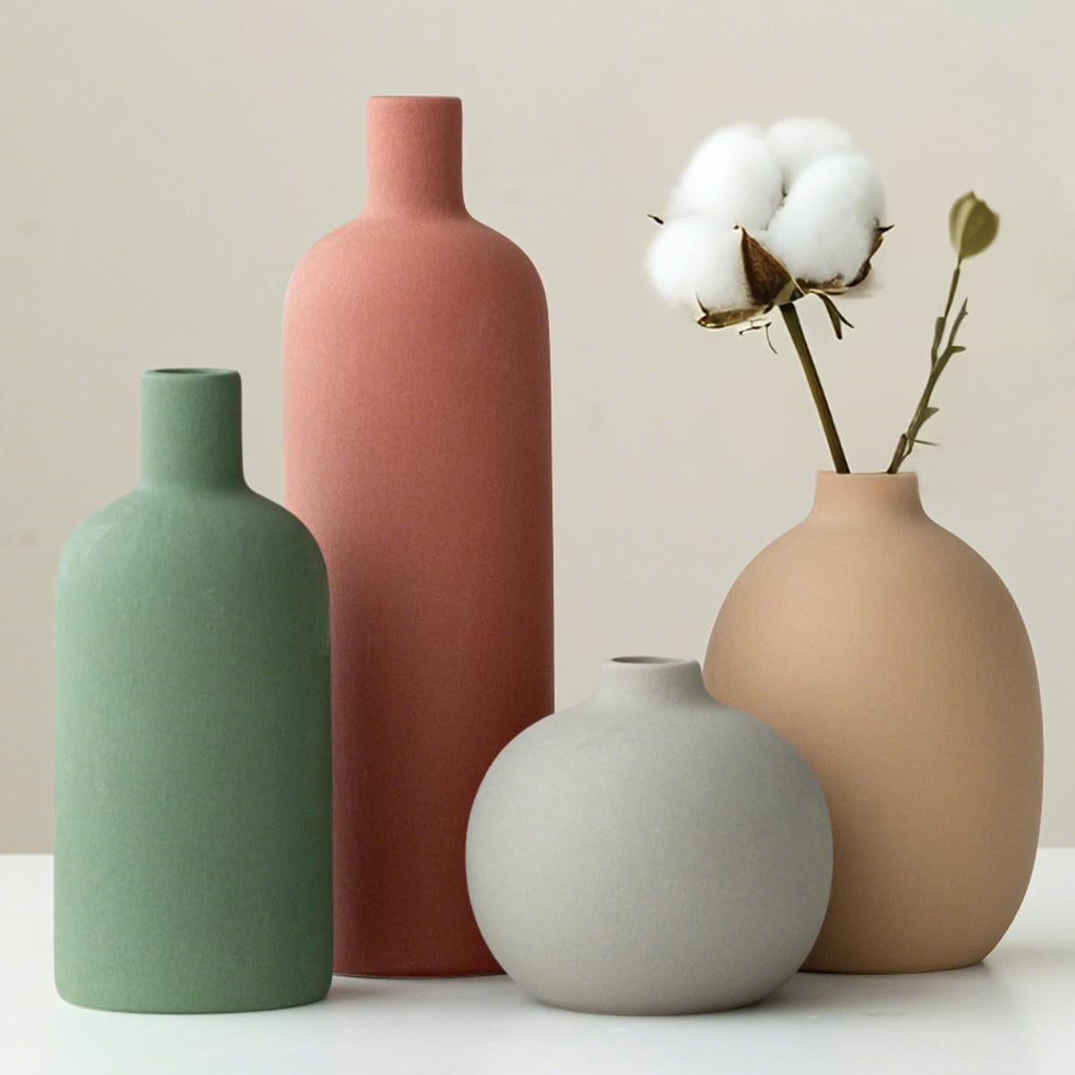 Close-up of four matte neutral vases with a tall terracotta vase and a cotton stem in the beige vase