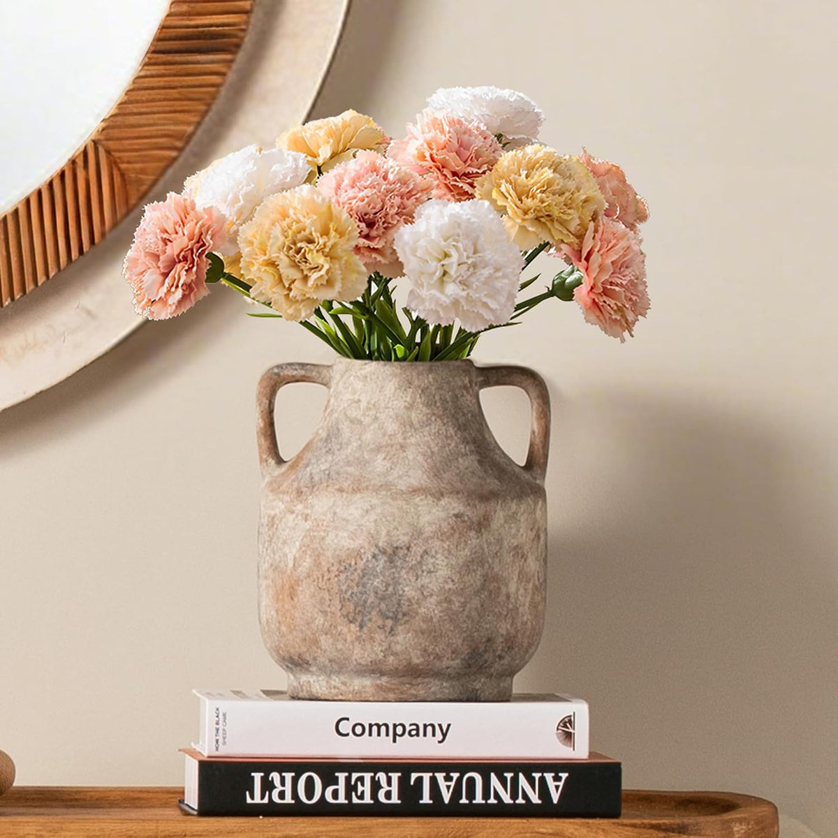 Front view of a short handled stone vase filled with pastel carnations, sitting on stacked books.