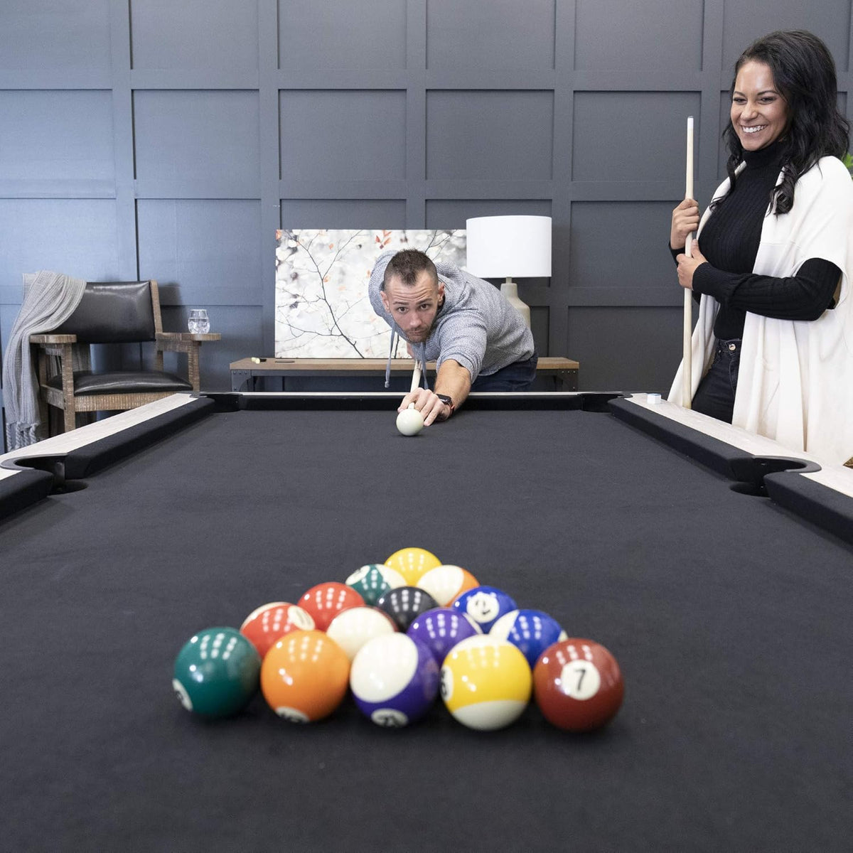 Low-angle view down the table toward a racked triangle of balls with a man lining up a break