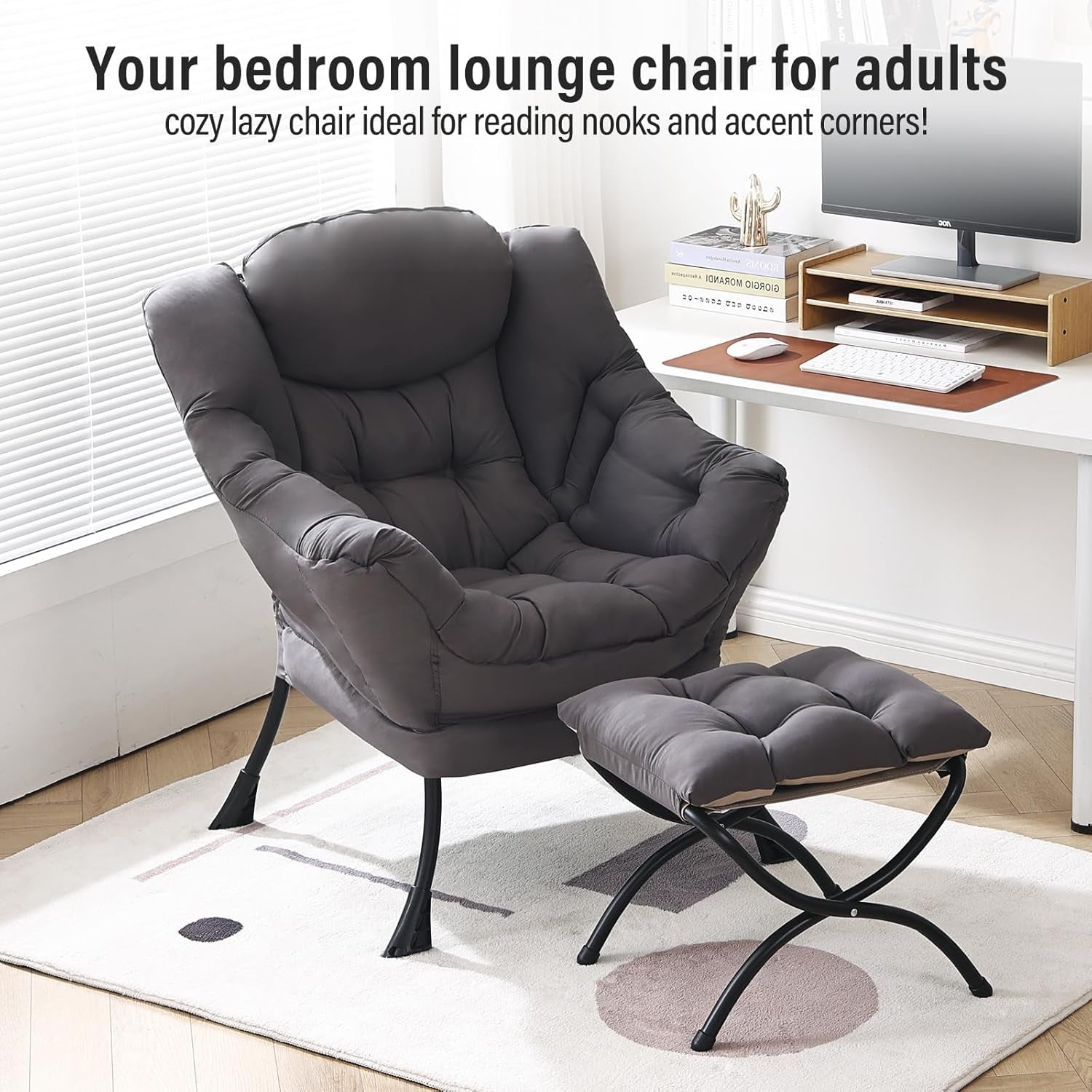 Dark grey lounge chair and ottoman placed beside a white desk and monitor in a sunny room on a patterned rug