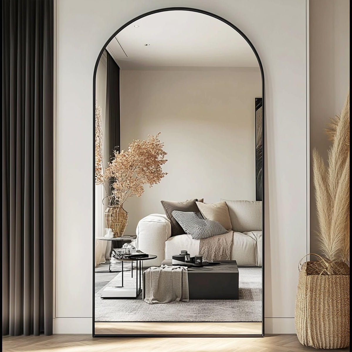 Tall arched mirror with a thin black frame leaning against a wall reflecting a sofa and coffee table.